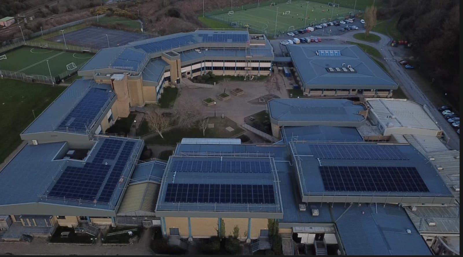 Aerial view of solar arrays across several roofs of an education site