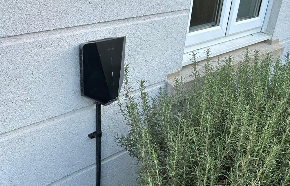 A black home EV charger neatly mounted on a house wall, with its cable clipped down to the ground